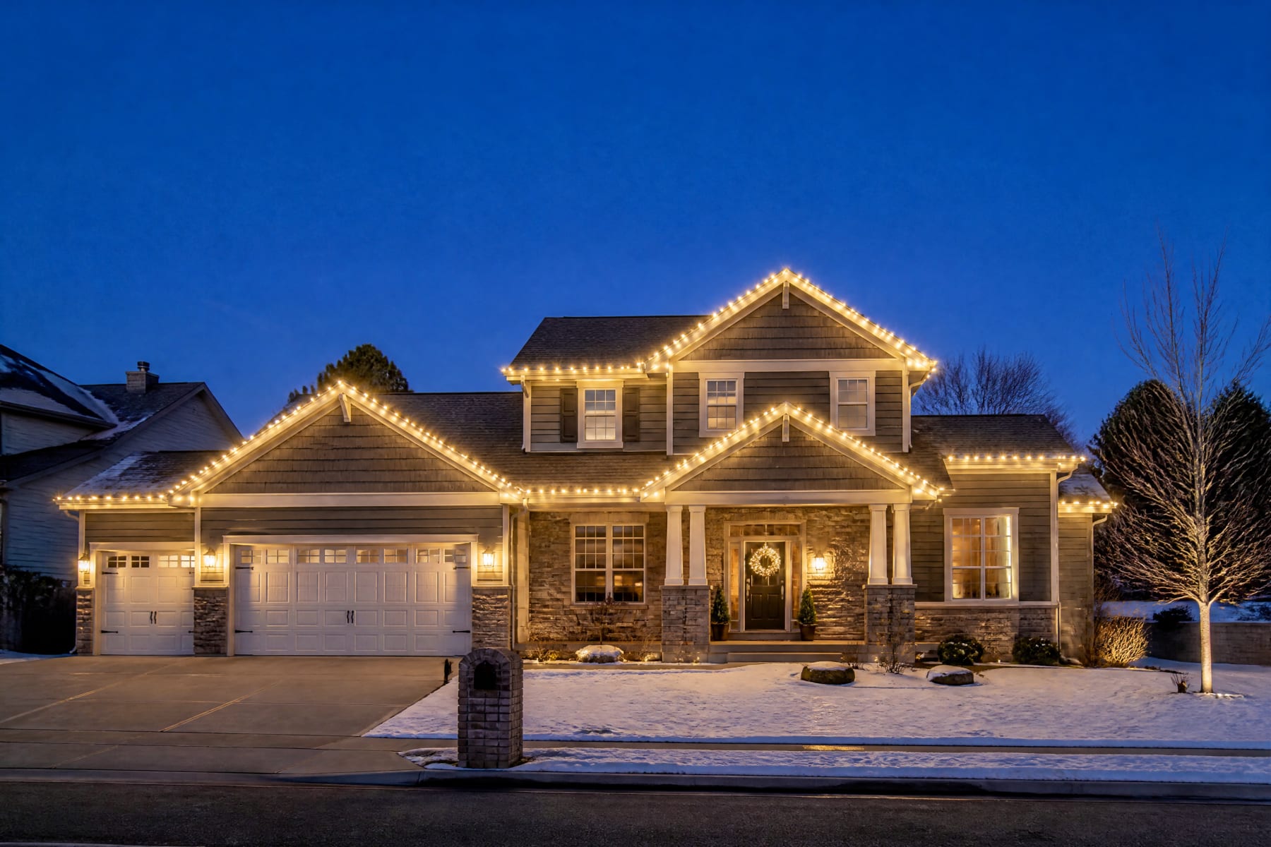 A two-story home at dusk with warm white lights on every roofline